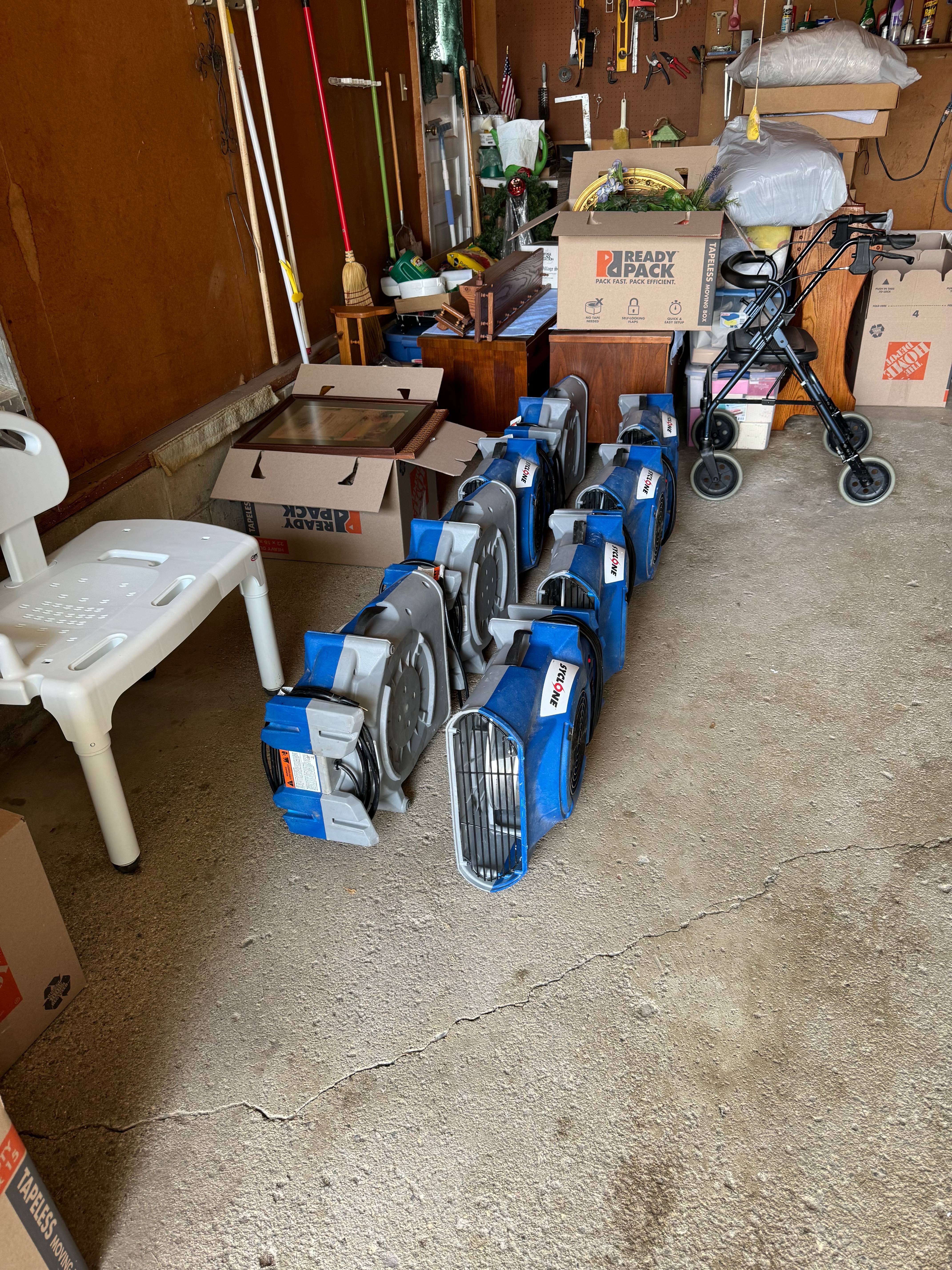 Multiple blue industrial air movers and fans lined up in garage for water damage drying and restoration work