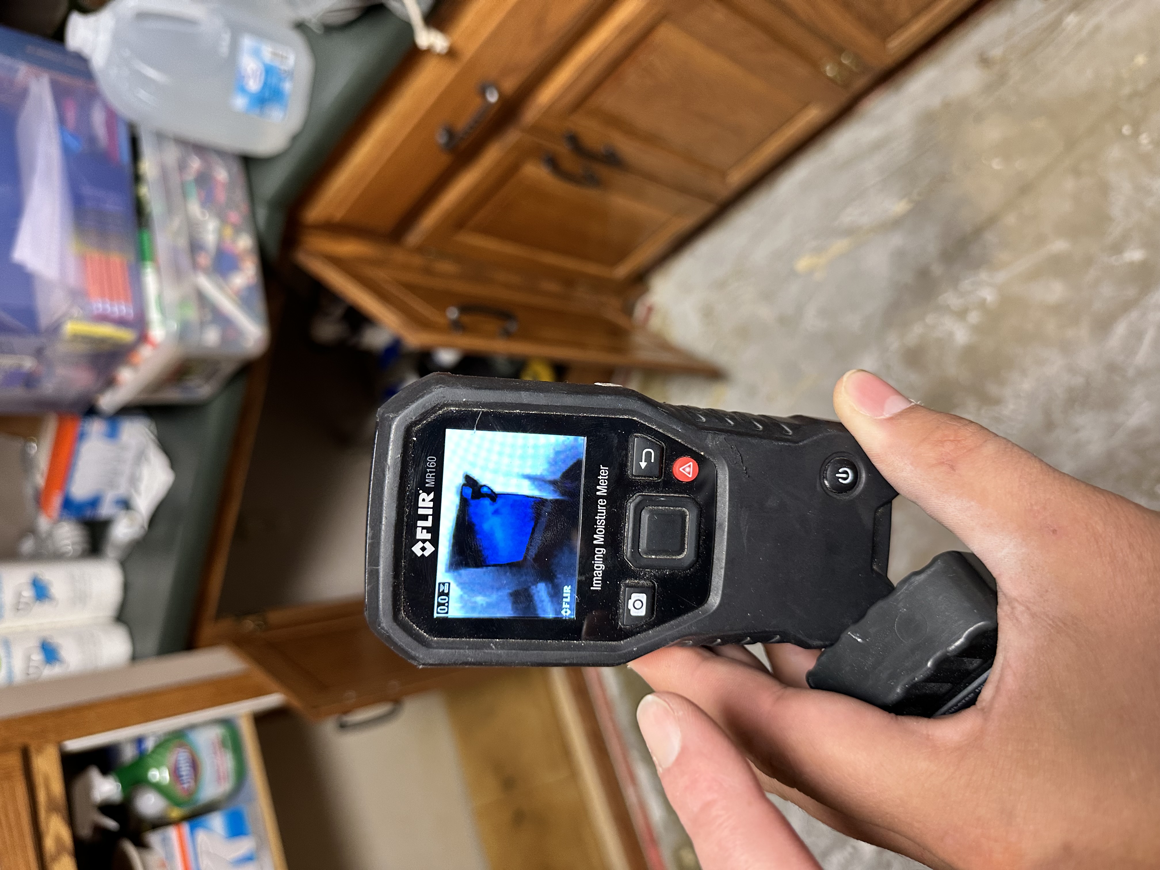FLIR MR160 Imaging Moisture Meter being held in hand displaying thermal imaging screen for professional moisture detection during water damage assessment