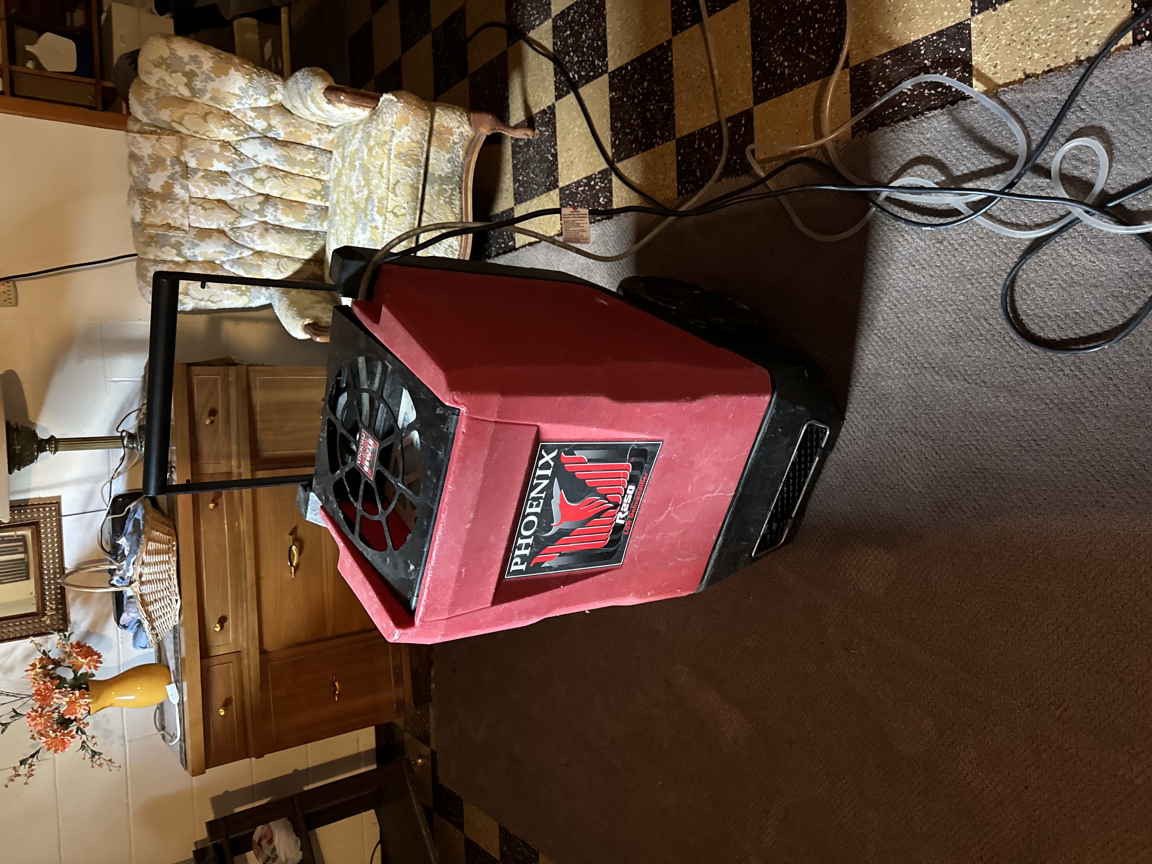 Red Phoenix brand dehumidifier and air scrubber unit positioned on checkered basement floor for professional moisture control during water damage restoration