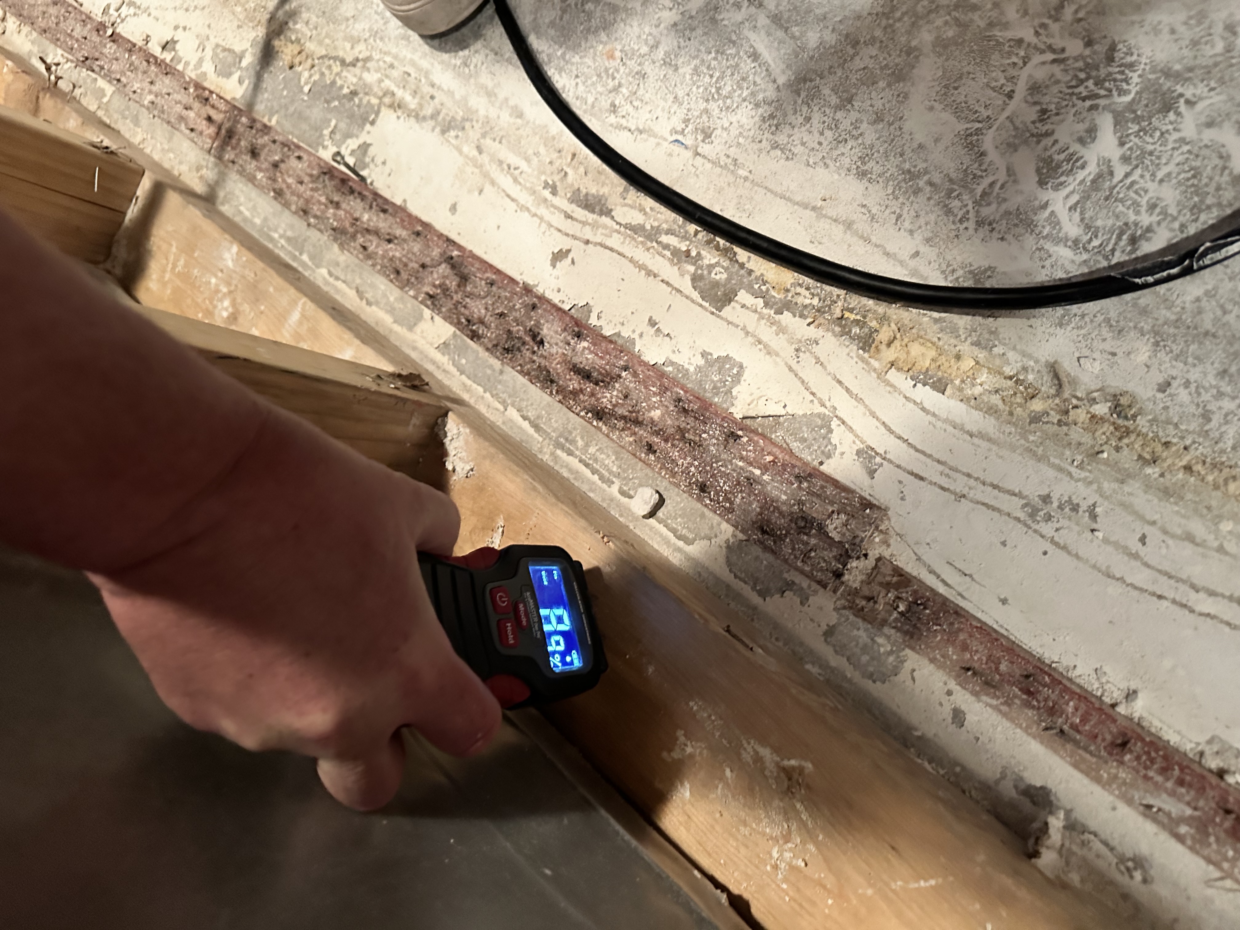Digital moisture meter displaying 6.0 reading being used to measure moisture levels in wooden floor materials during water damage assessment