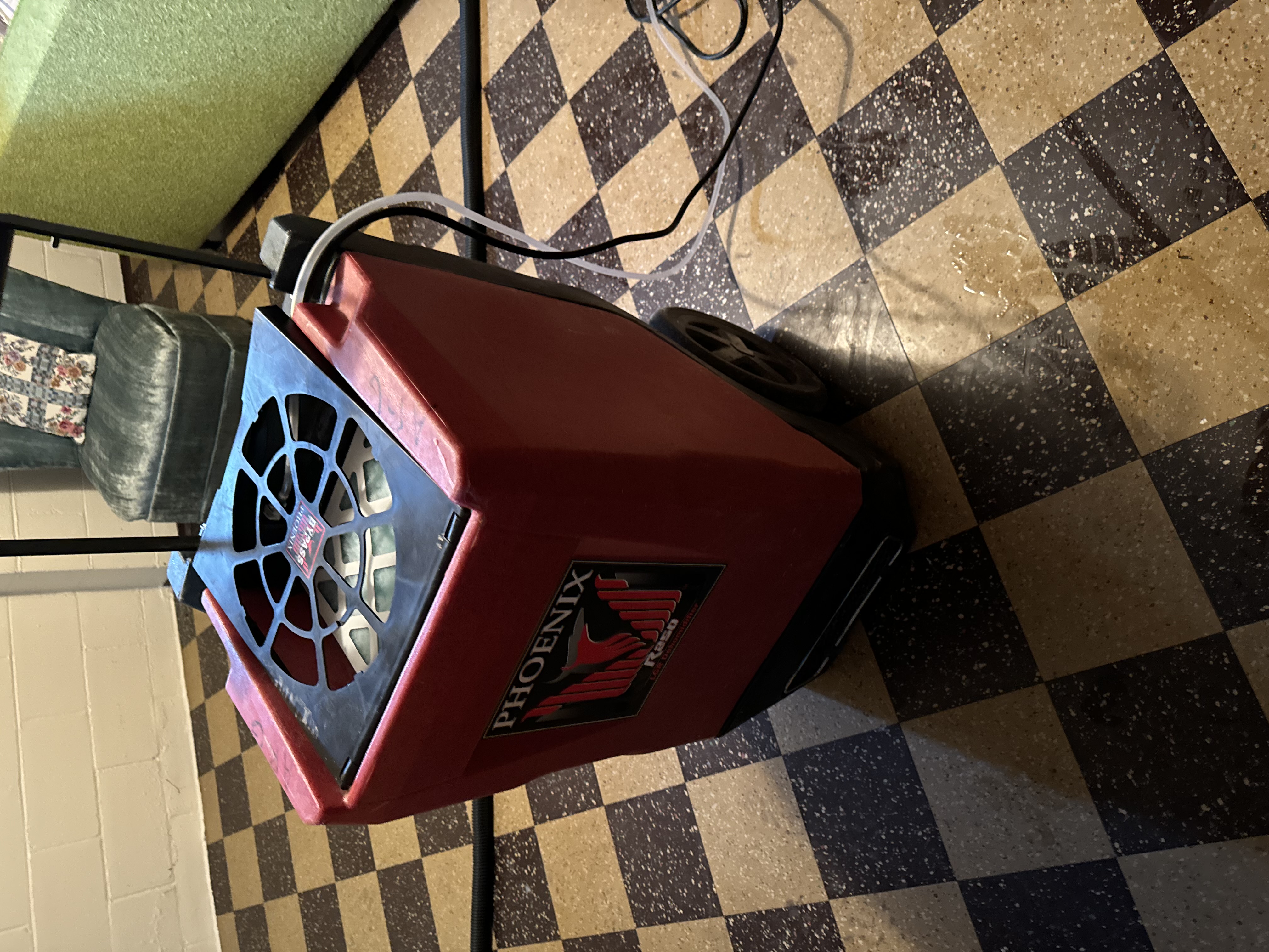 Red Phoenix dehumidifier unit positioned on checkered basement floor for structural drying during professional water damage restoration