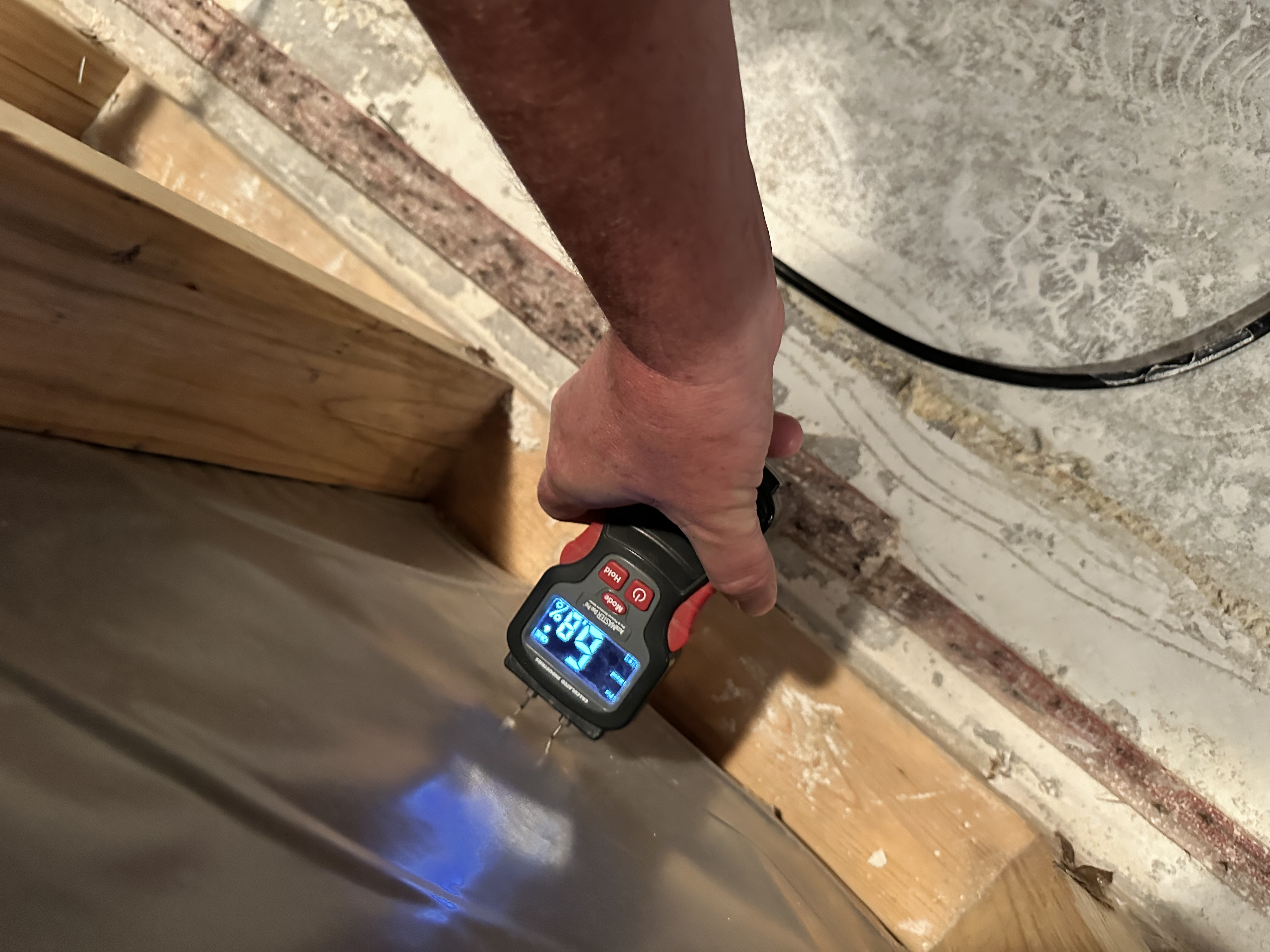 Digital moisture meter displaying 39.7 reading being used to test moisture levels in wooden structural materials during water damage assessment