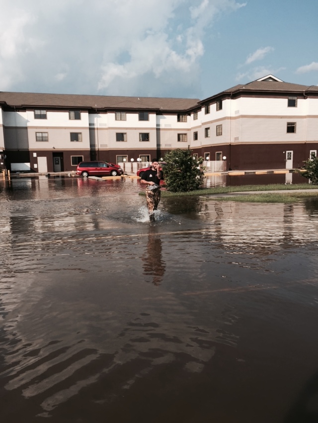 Major flood emergency at apartment complex with person wading through knee-deep flood water in parking area requiring immediate emergency water damage response