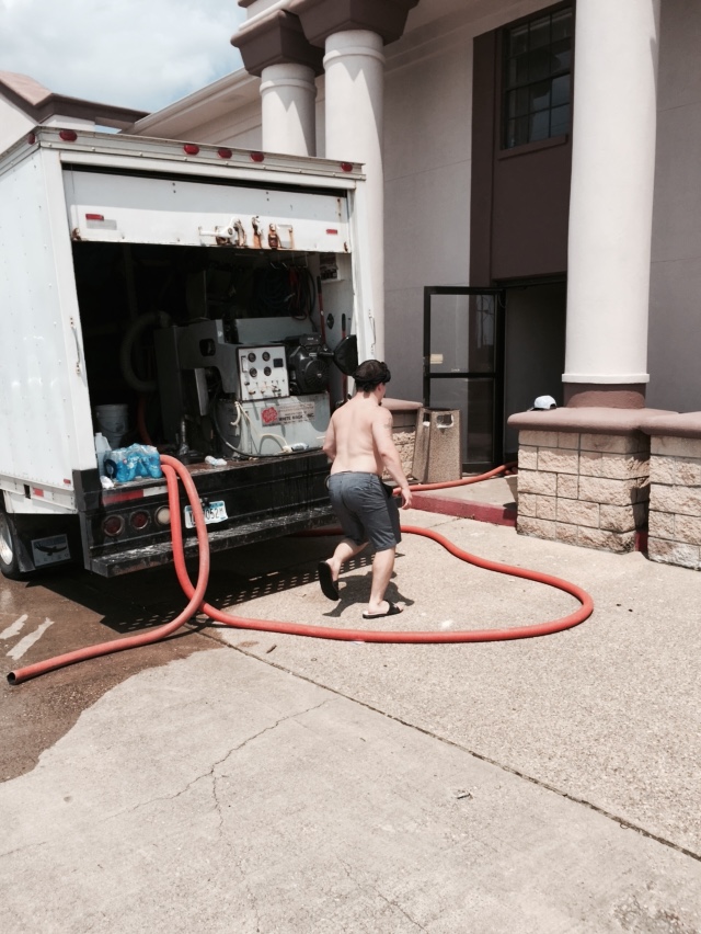 Professional water extraction truck with technician working with large orange hoses connected to truck-mounted equipment at commercial building with columns