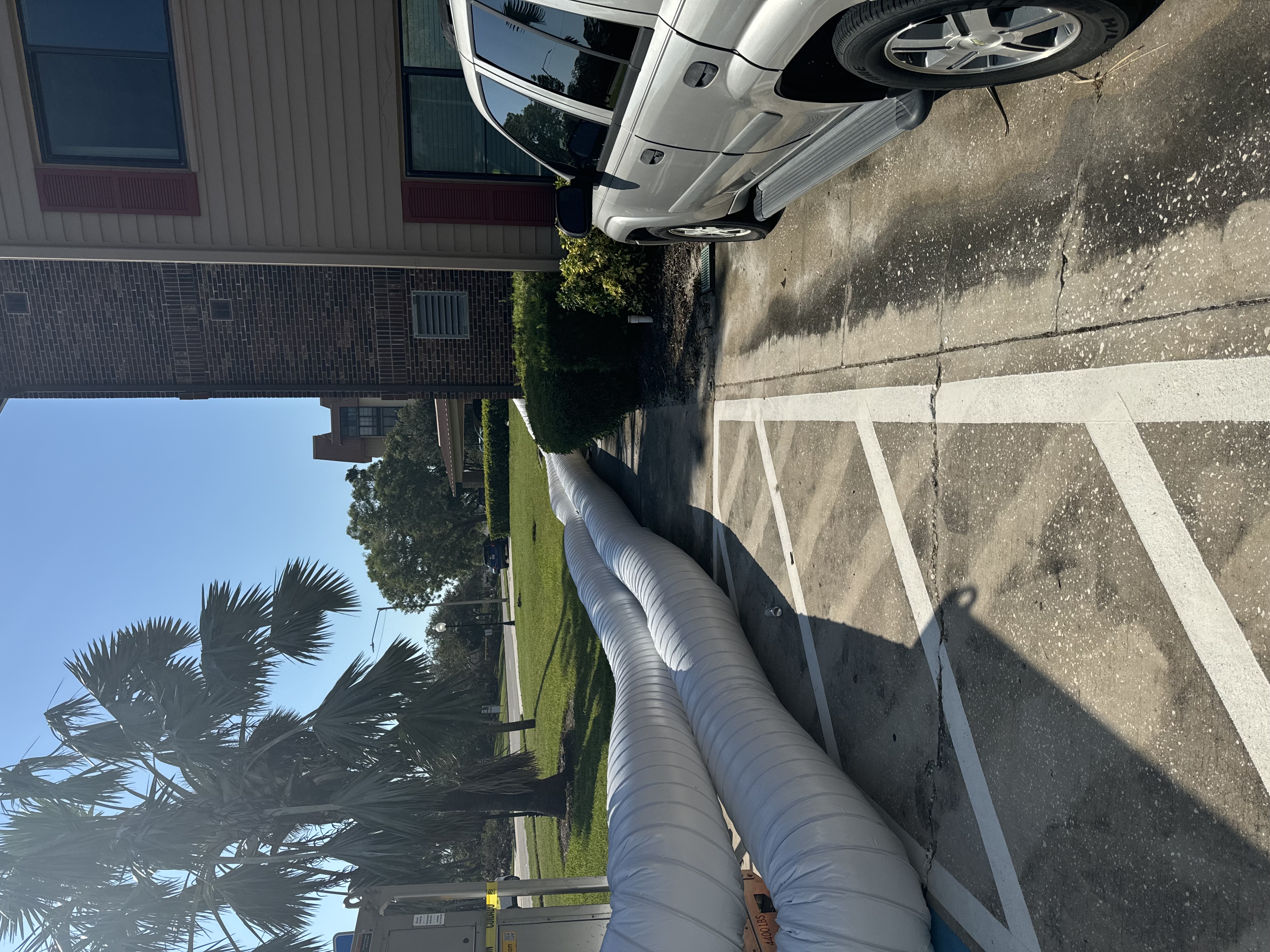Large white flexible ducting laid across Woodbury parking lot near residential buildings for water damage restoration operations