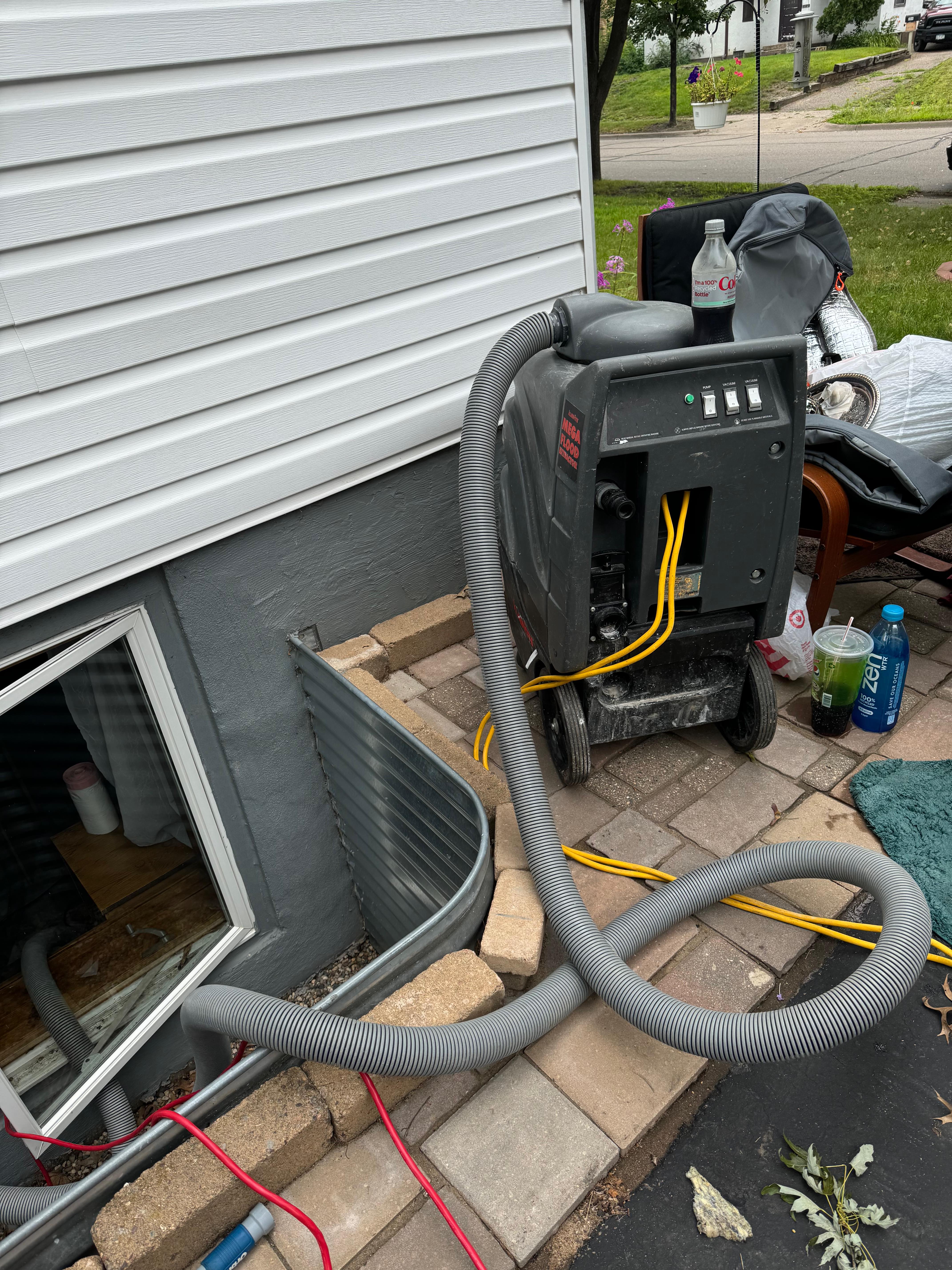 Professional water damage restoration equipment including large industrial dehumidifier with gray flexible hoses on residential patio next to white siding