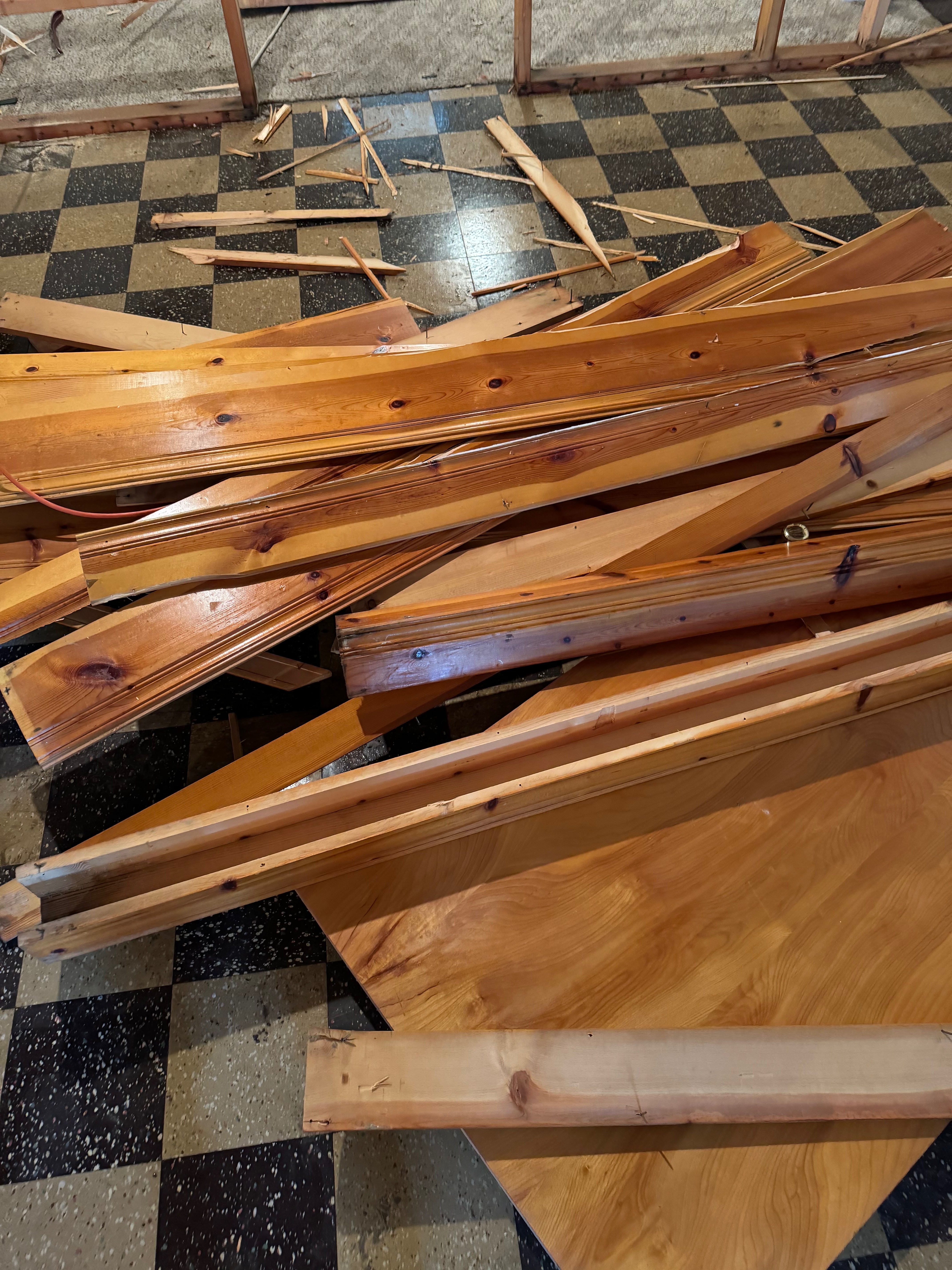 Water-damaged wooden flooring and lumber pieces scattered on checkered floor showing flood damage requiring removal and replacement